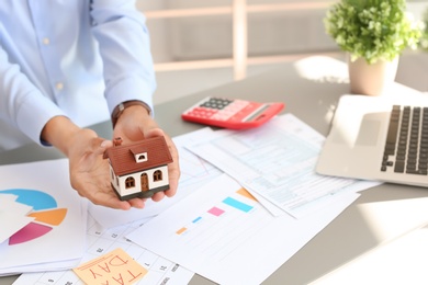 Man holding house model at table, closeup. Property tax