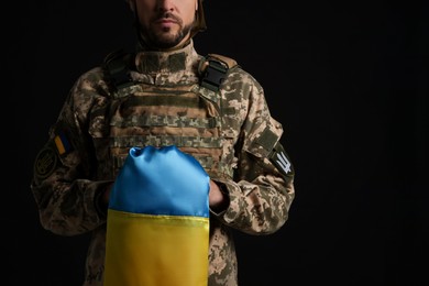 Soldier in military uniform with Ukrainian flag on black background, closeup