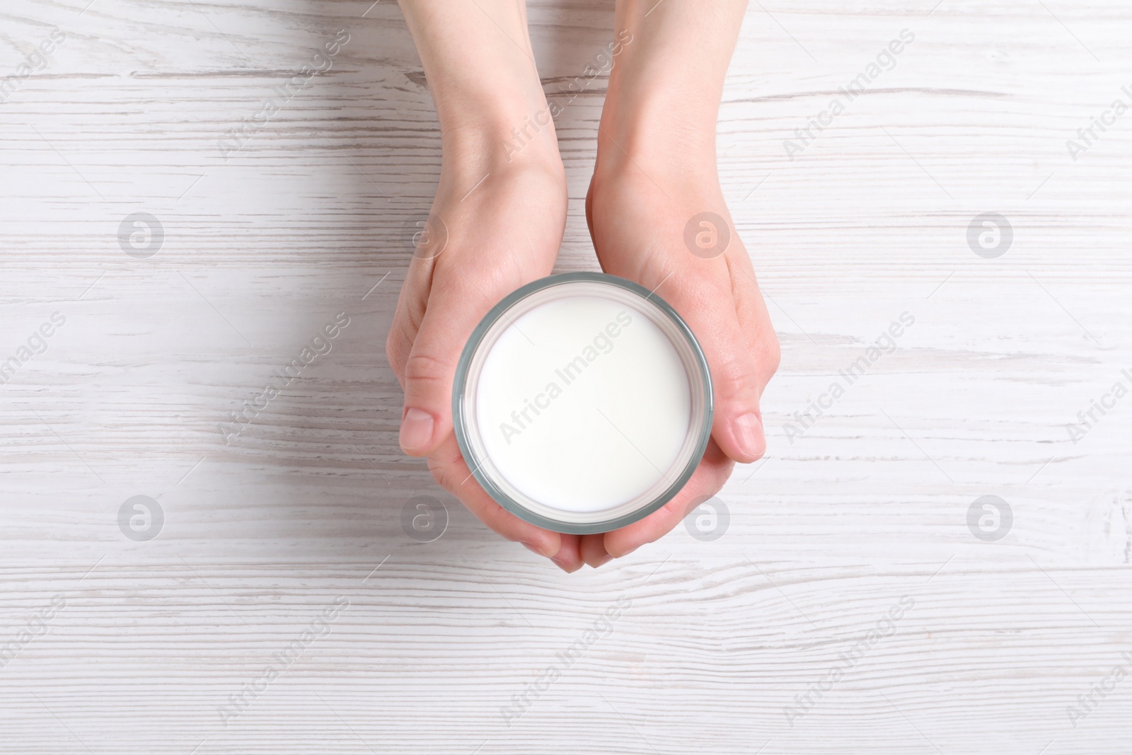 Photo of Woman holding glass of milk at white wooden table, top view