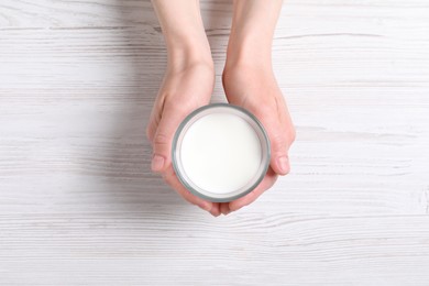 Photo of Woman holding glass of milk at white wooden table, top view