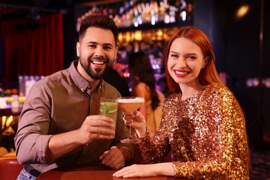 Photo of Happy couple clinking glasses with fresh cocktails at table in bar