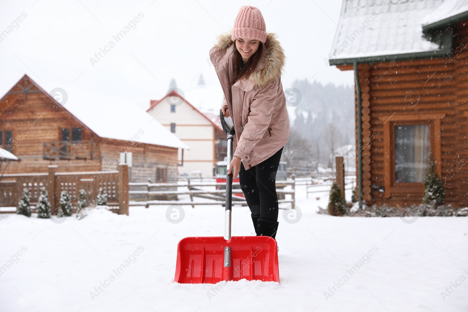 Photo of Young woman cleaning snow with shovel near her house