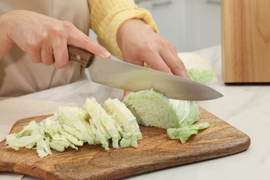 Photo of Woman cutting fresh chinese cabbage at table in kitchen, closeup