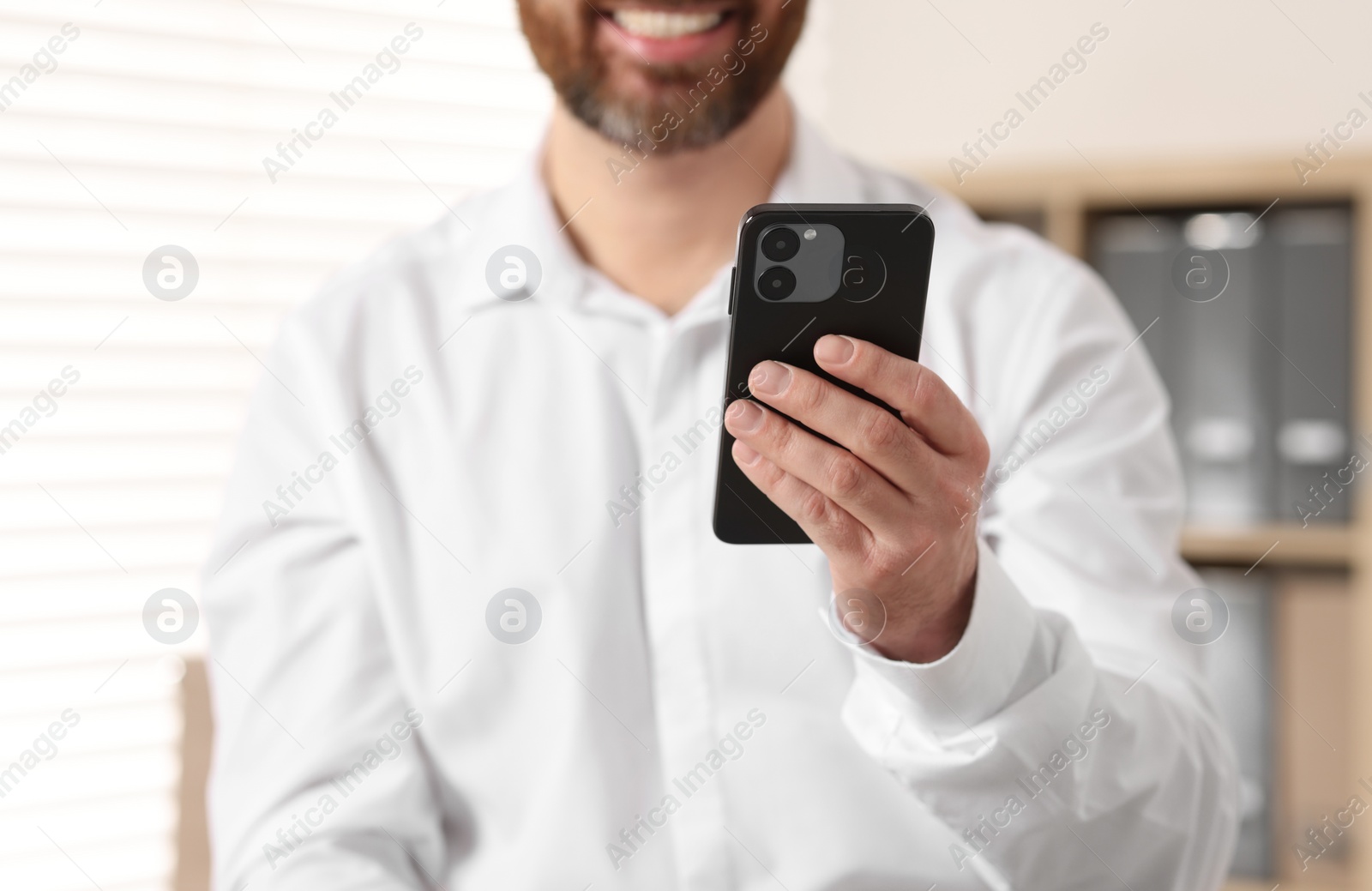 Photo of Smiling man using smartphone in office, closeup