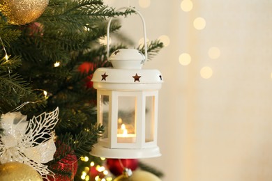 Christmas lantern with burning candle and balls on fir tree indoors, closeup