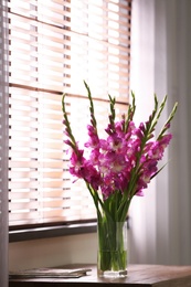 Photo of Vase with beautiful pink gladiolus flowers on wooden table in room, space for text