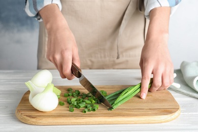 Photo of Woman cutting fresh green onion on wooden board at table, closeup