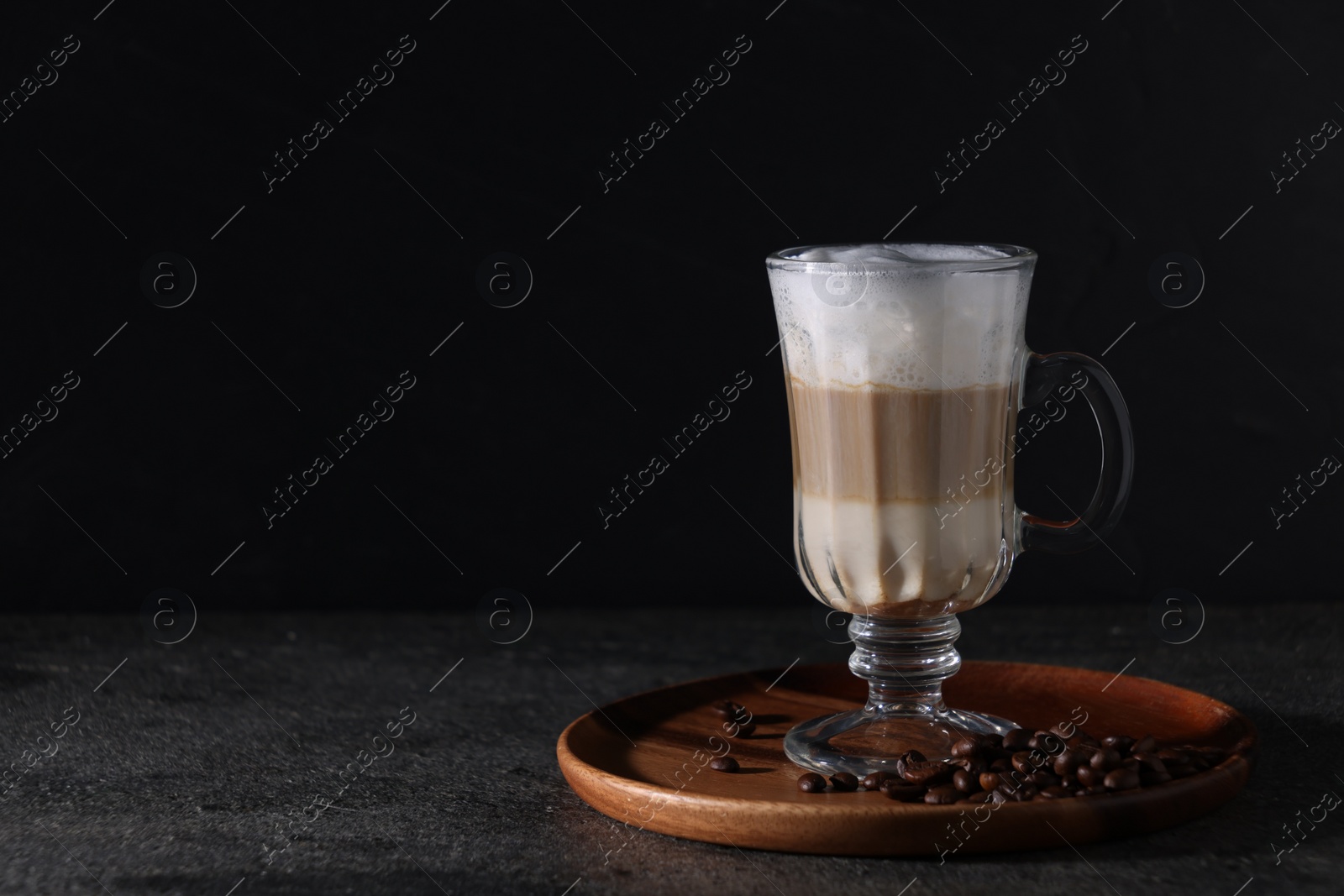 Photo of Aromatic latte macchiato in glass and coffee beans on dark grey table. Space for text