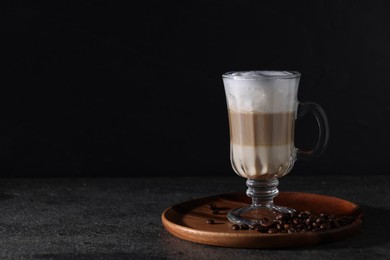 Photo of Aromatic latte macchiato in glass and coffee beans on dark grey table. Space for text