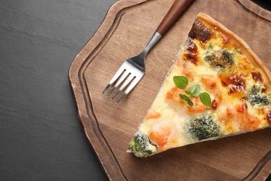 Piece of delicious homemade salmon quiche with broccoli and fork on black table, top view. Space for text