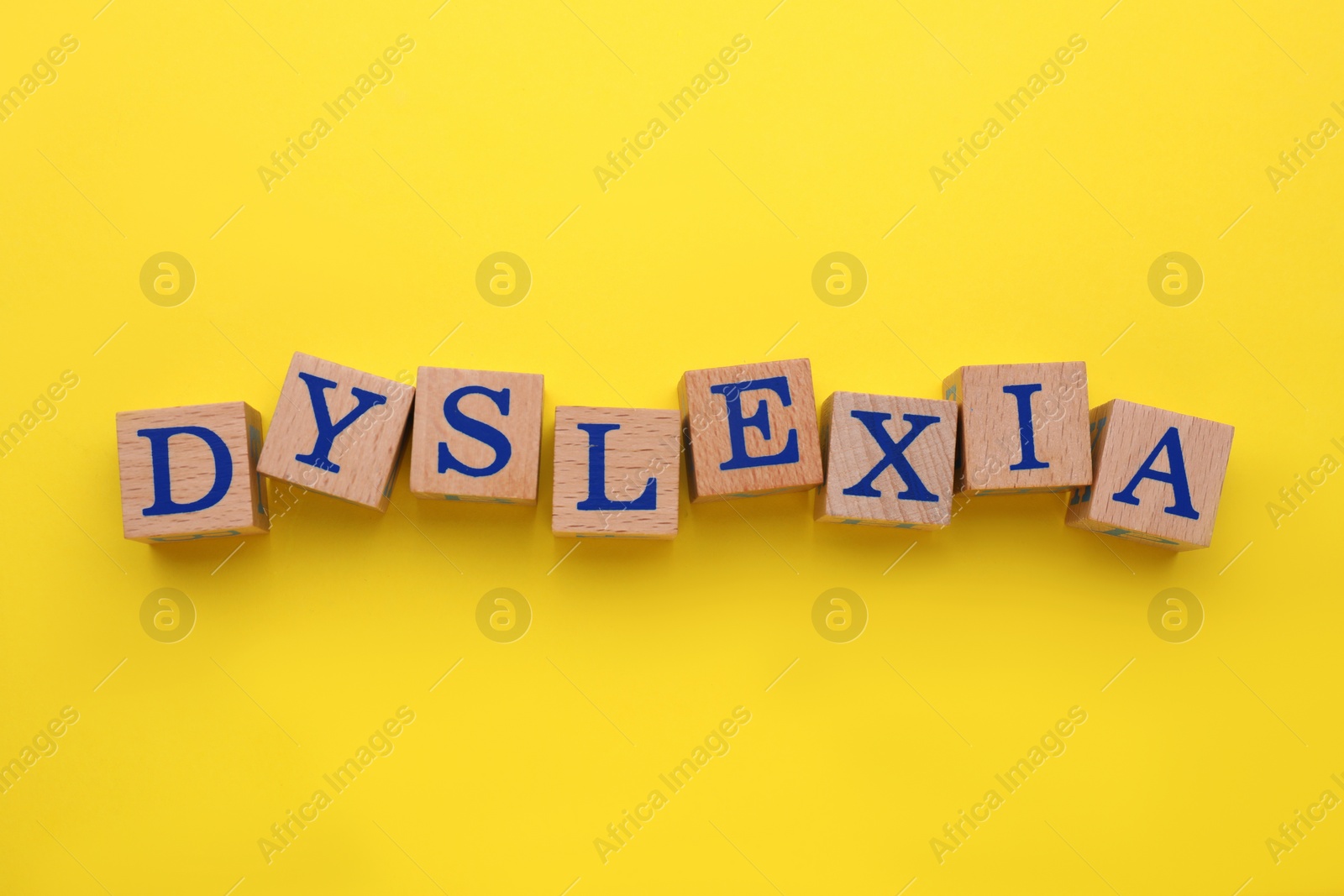 Photo of Wooden cubes with word Dyslexia on yellow background, flat lay