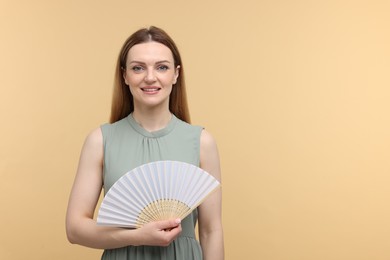 Happy woman with hand fan on beige background, space for text