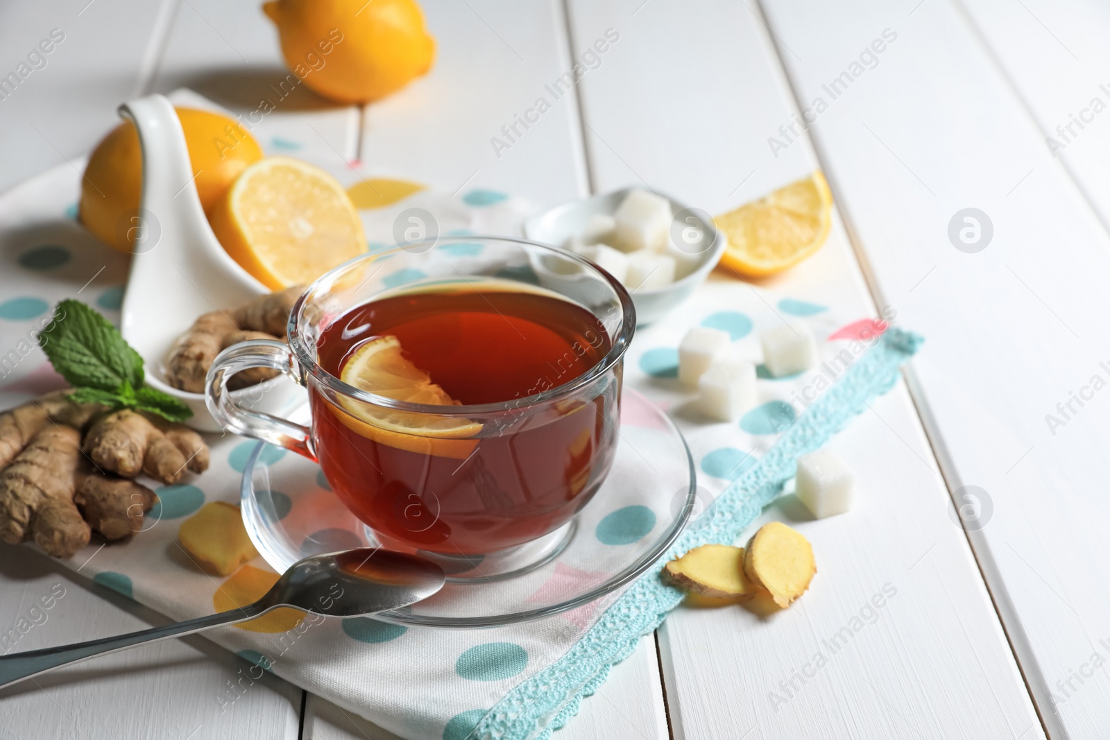 Photo of Cup of delicious ginger tea, sugar cubes and lemons on white wooden table