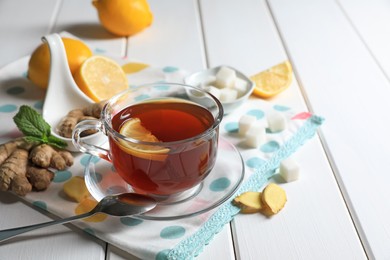 Cup of delicious ginger tea, sugar cubes and lemons on white wooden table