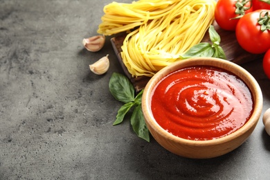 Photo of Bowl of tasty tomato sauce and pasta served on grey table. Space for text