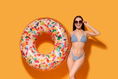 Young woman with stylish sunglasses holding inflatable ring against orange background