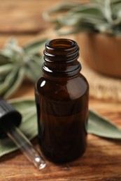 Photo of Bottle of essential sage oil, dropper and leaves on wooden table, closeup