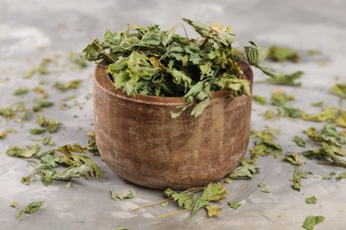 Photo of Bowl with dry parsley on light grey textured table, closeup