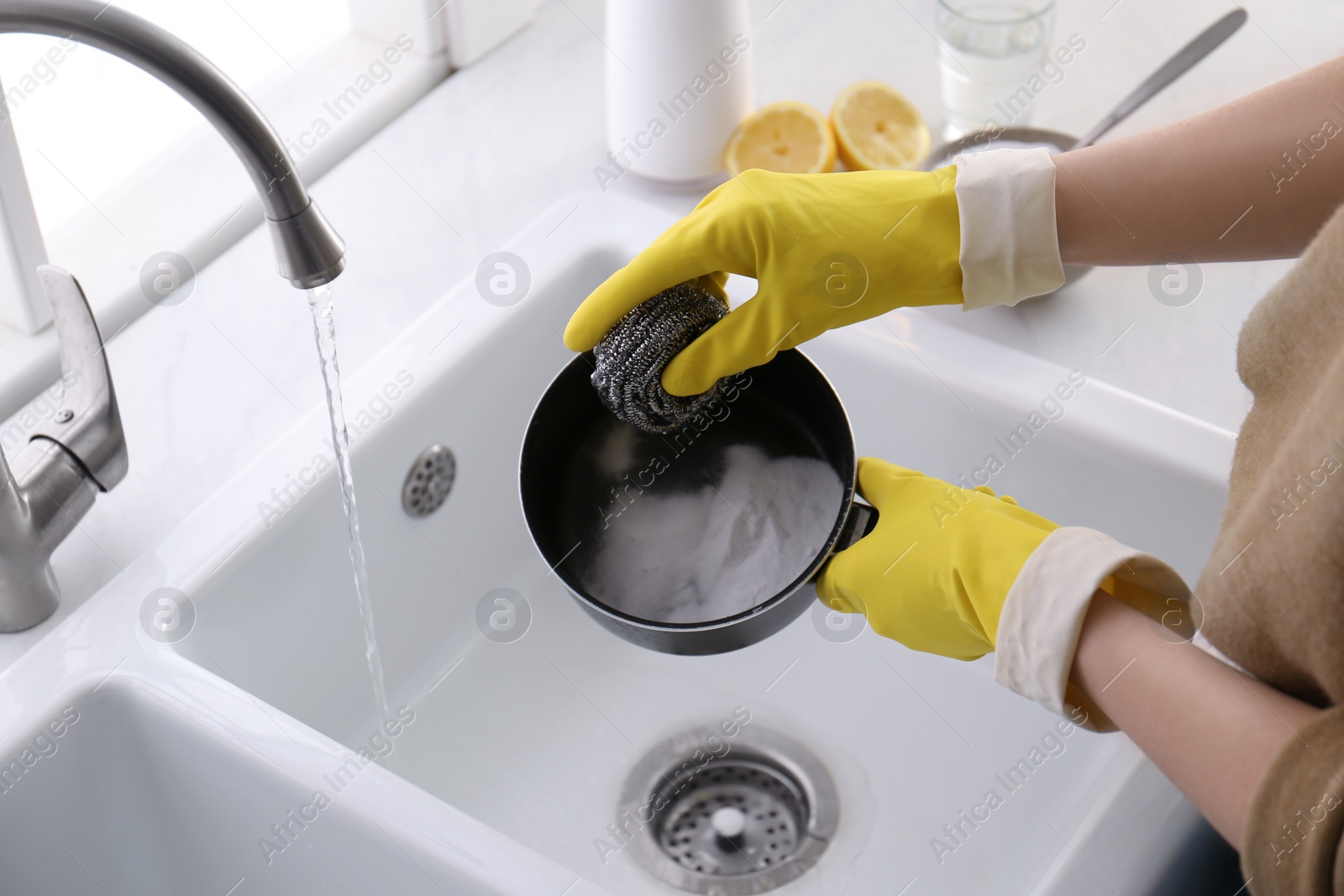 Photo of Woman using baking soda and metal sponge to clean pot, closeup