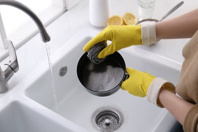 Photo of Woman using baking soda and metal sponge to clean pot, closeup