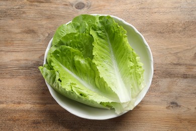 Photo of Bowl with fresh leaves of green romaine lettuce on wooden table, top view