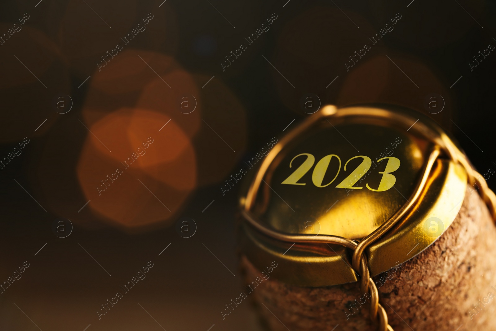Image of Cork of sparkling wine and muselet cap with engraving 2023 against blurred festive lights, closeup. Bokeh effect