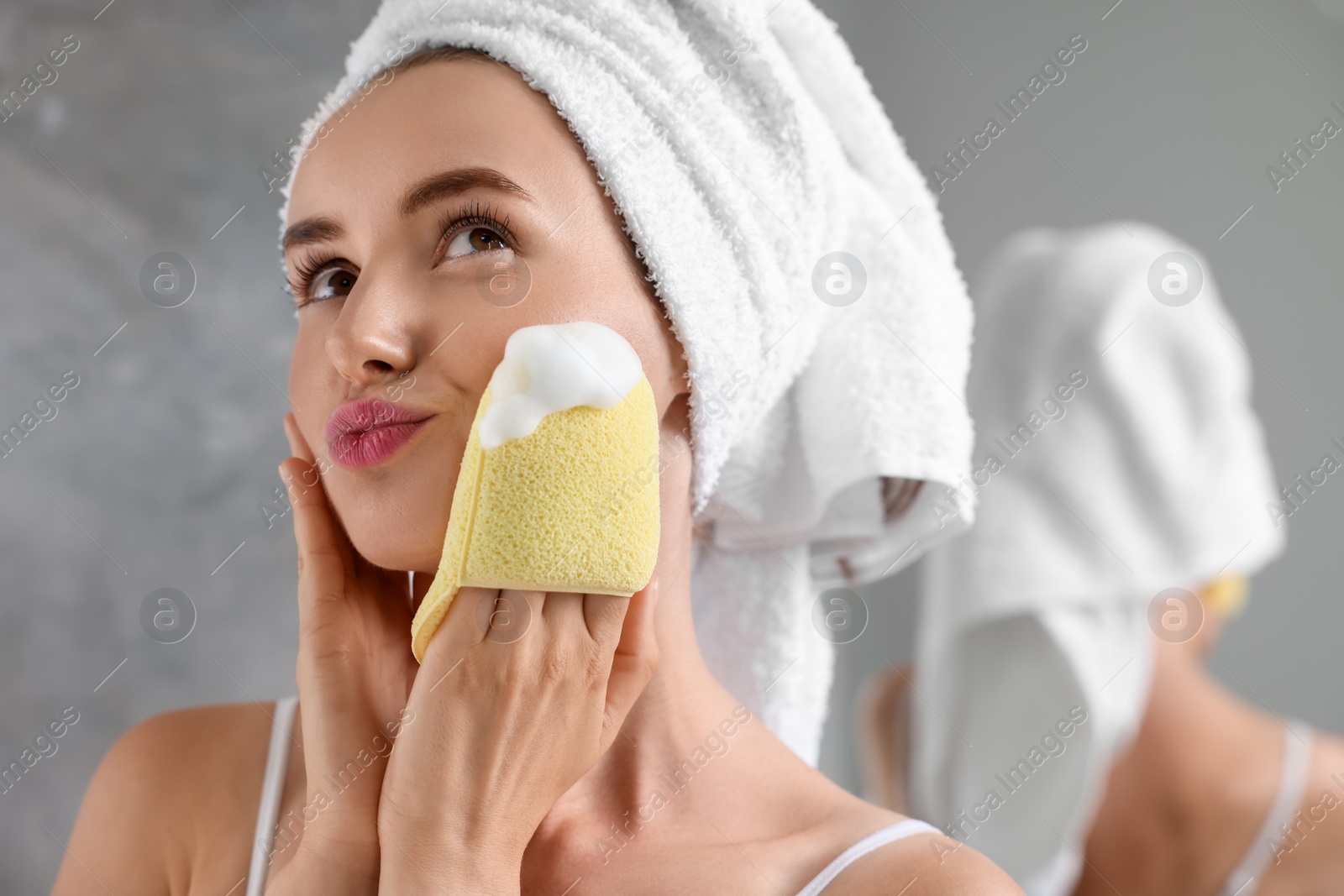 Photo of Happy young woman washing her face with sponge in bathroom