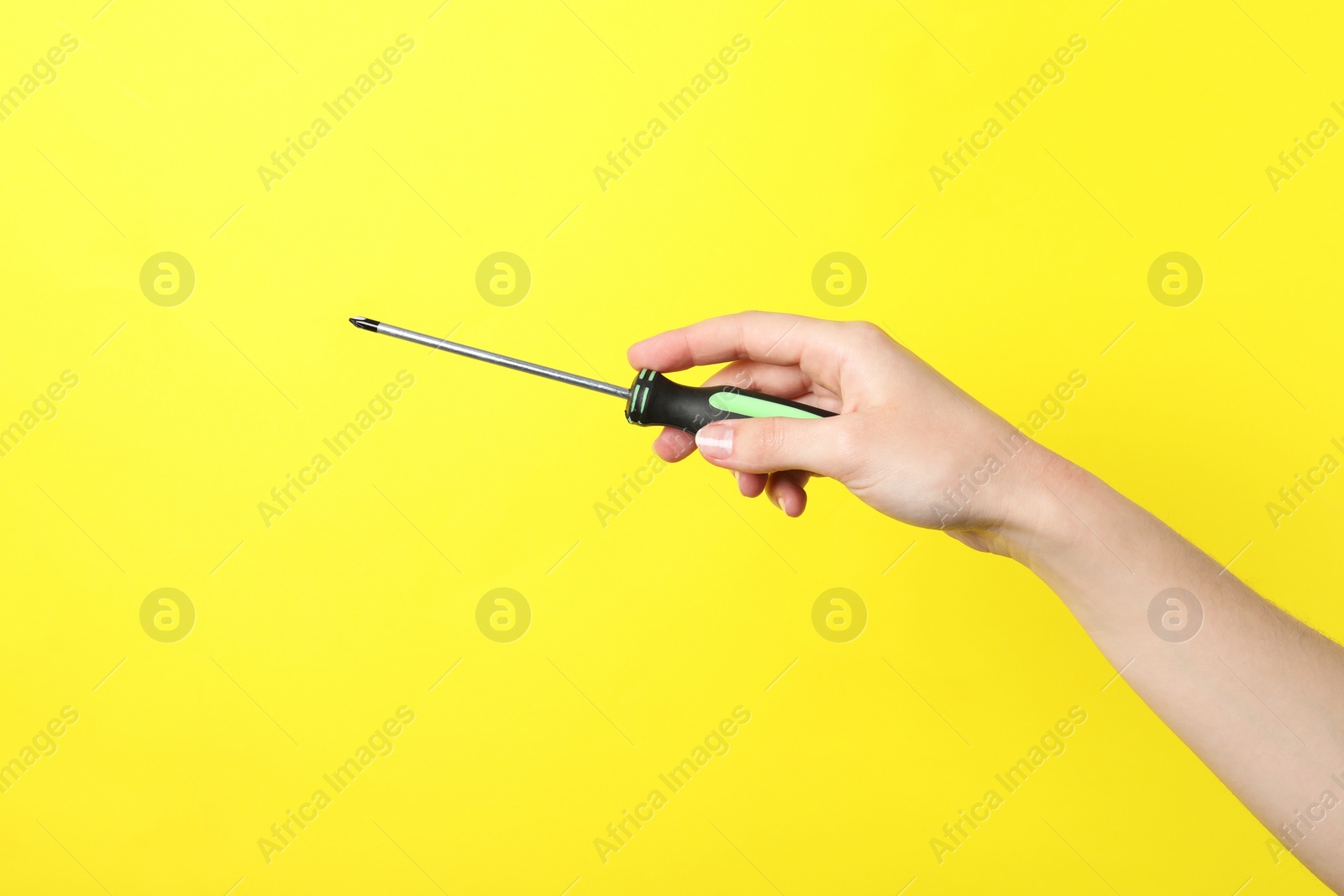 Photo of Woman holding screwdriver on yellow background, closeup. Space for text