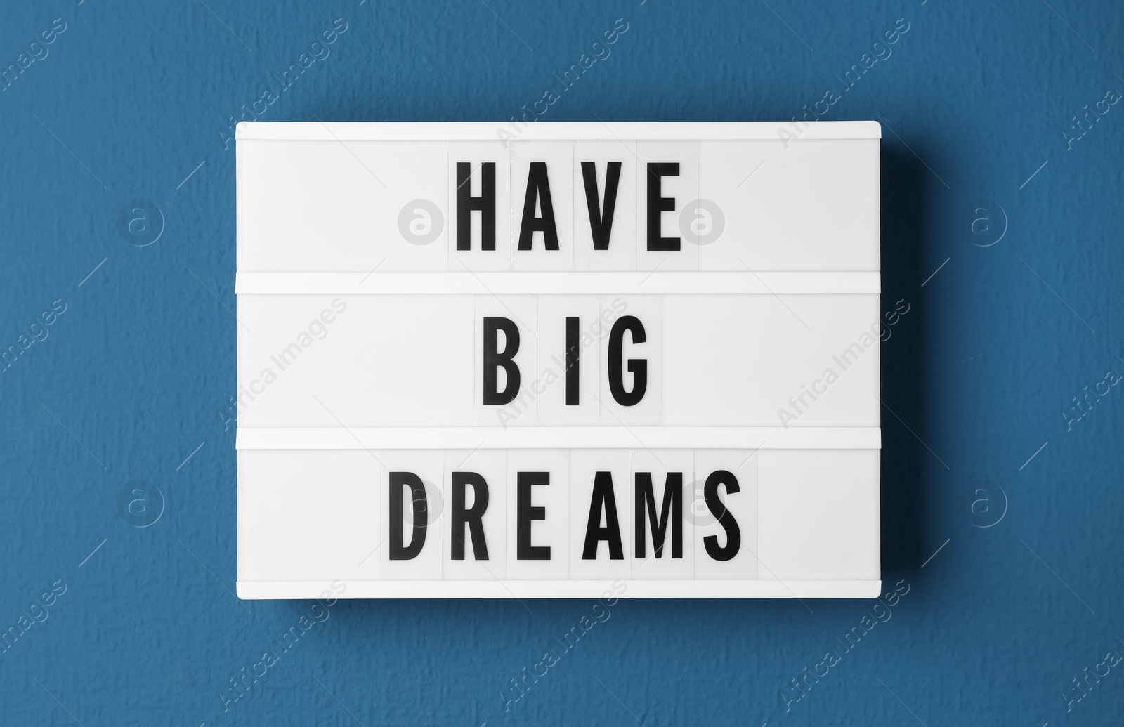 Photo of Lightbox with motivational quote Have Big Dreams on blue background, top view