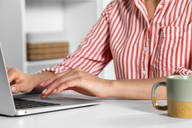 Photo of Young woman working with laptop at workplace indoors, closeup