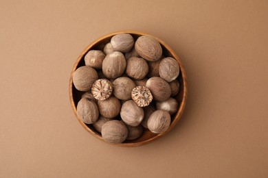 Photo of Nutmegs in wooden bowl on light brown background, top view