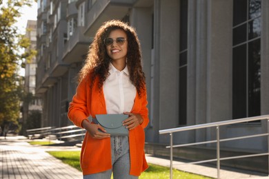 Beautiful African American woman with stylish waist bag on city street, space for text