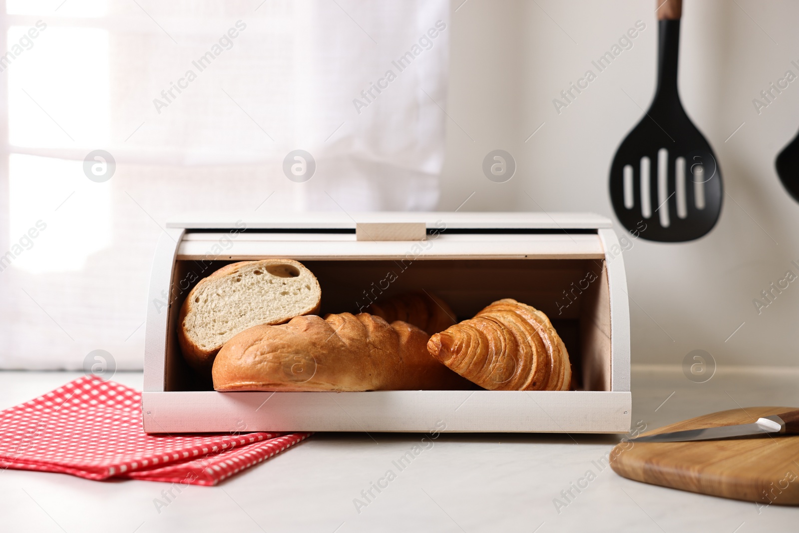 Photo of Wooden bread basket with freshly baked loaves on white marble table in kitchen