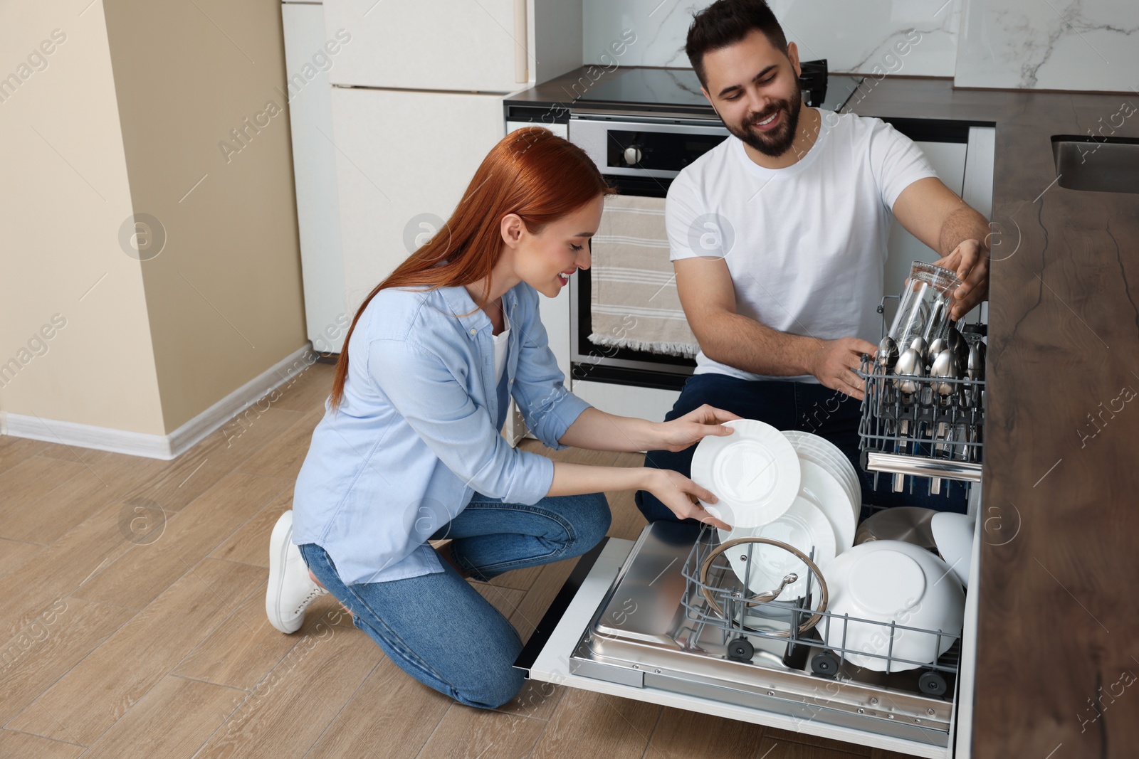 Photo of Happy couple loading dishwasher with plates in kitchen