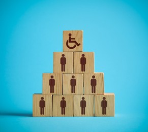 Image of Inclusive workplace culture. Pyramid of wooden cubes with human icons and one with international symbol of access on light blue background