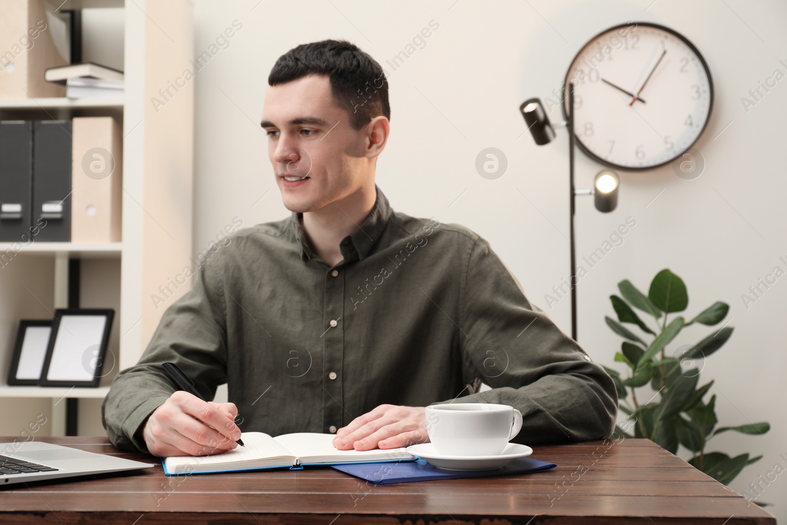 Photo of Man taking notes at wooden table in office