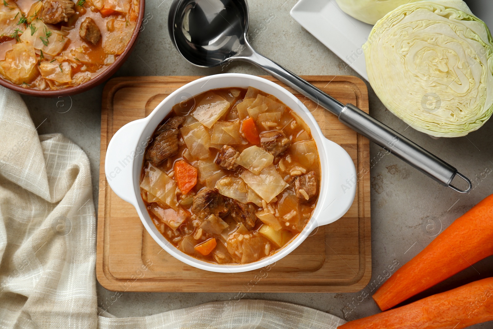 Photo of Tasty cabbage soup and ingredients on light grey textured table, flat lay