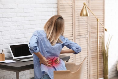 Woman suffering from pain in lower back at table indoors