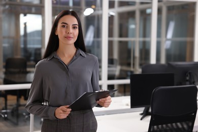 Beautiful woman with clipboard in office, space for text. Lawyer, businesswoman, accountant or manager