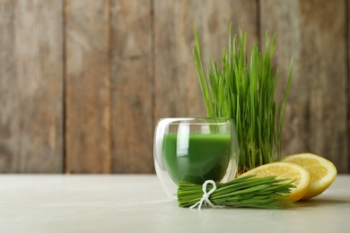 Photo of Glass of wheat grass juice with citrus fruit and sprouts on table. Space for text
