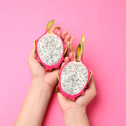 Photo of Woman holding halves of delicious ripe dragon fruit (pitahaya) on pink background