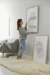 Photo of Woman hanging picture on wall in room. Interior design