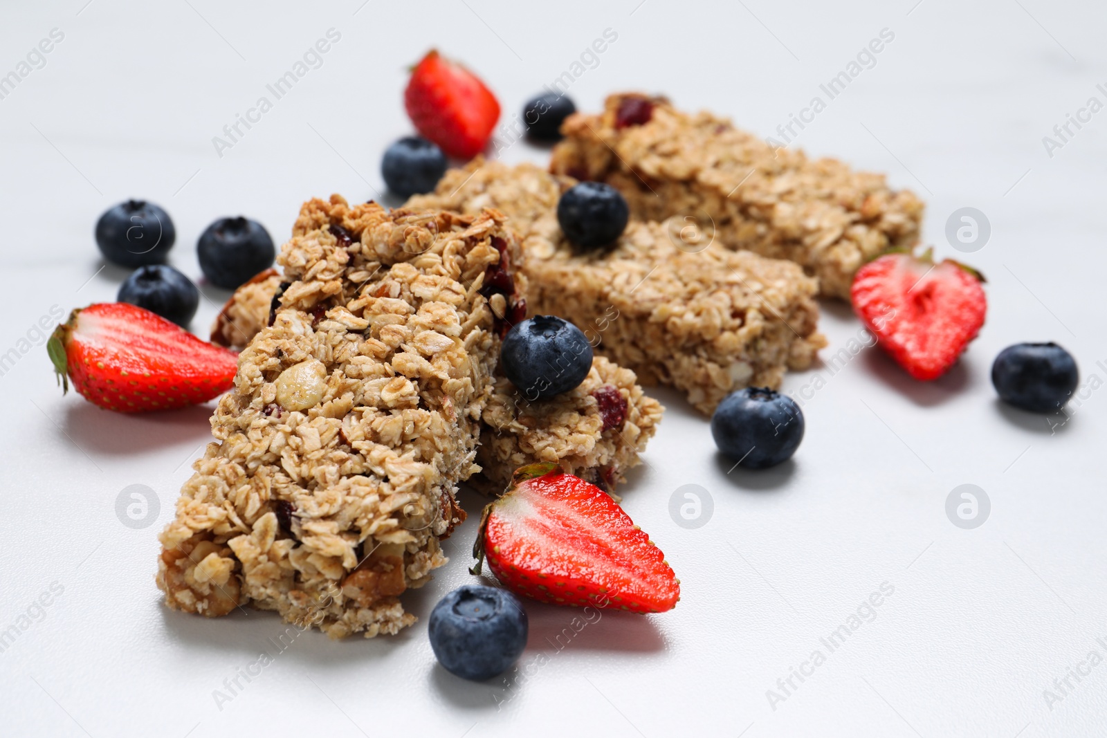 Photo of Tasty granola bars and berries on white table, closeup