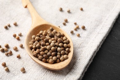 Photo of Spoon with dried coriander seeds and light cloth on dark gray table, closeup