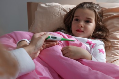 Photo of Doctor with thermometer near little girl in bed indoors