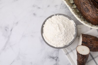 Photo of Bowl with cassava flour and roots on white marble table, flat lay. Space for text
