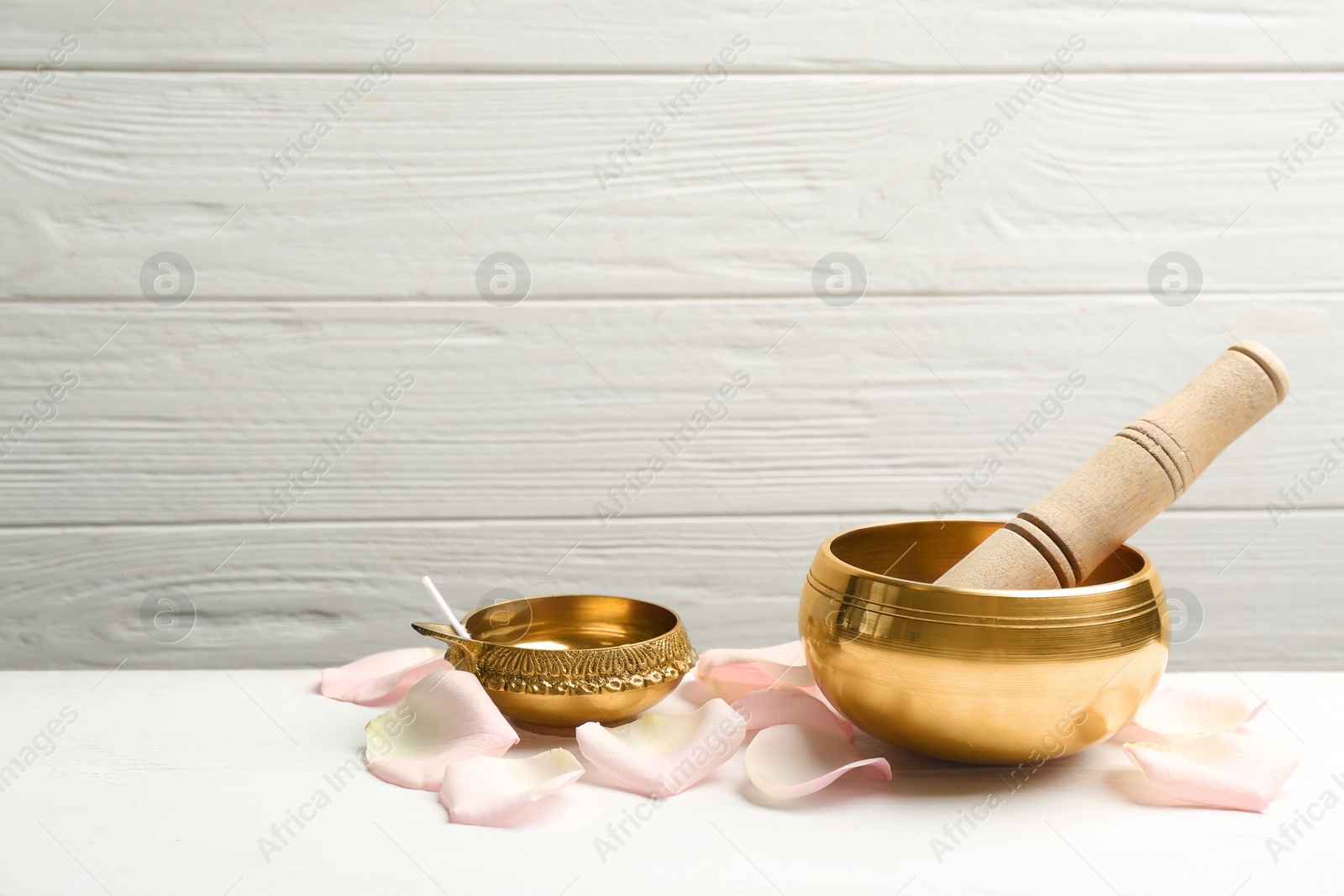 Photo of Composition with golden singing bowl and petals on white wooden table, space for text. Sound healing
