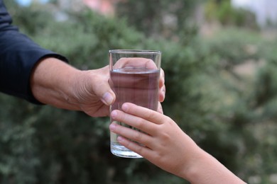 Child giving glass of water to elderly woman outdoors, closeup