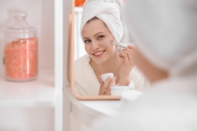 Woman applying scrub onto face in front of mirror at home