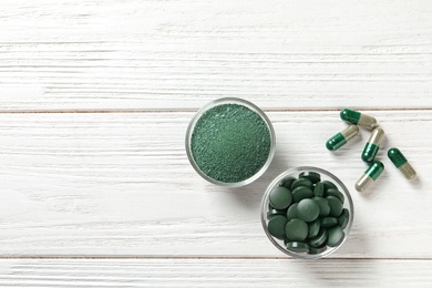 Photo of Bowls of spirulina pills and powder on wooden background, top view. Space for text